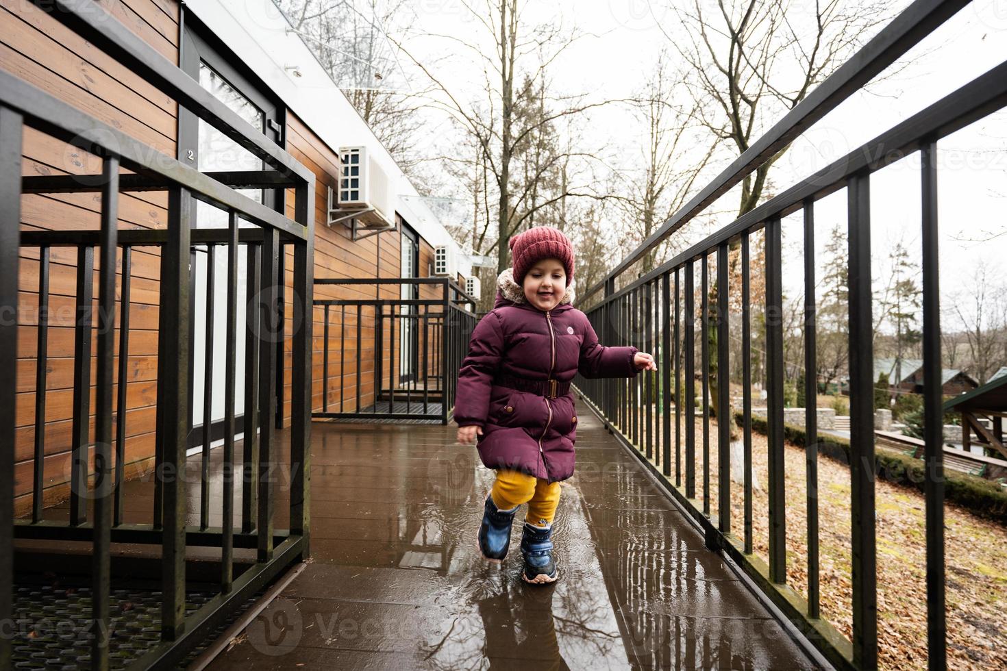 Baby girl running on terrace of one-storey modular houses in spring rainy forest. photo