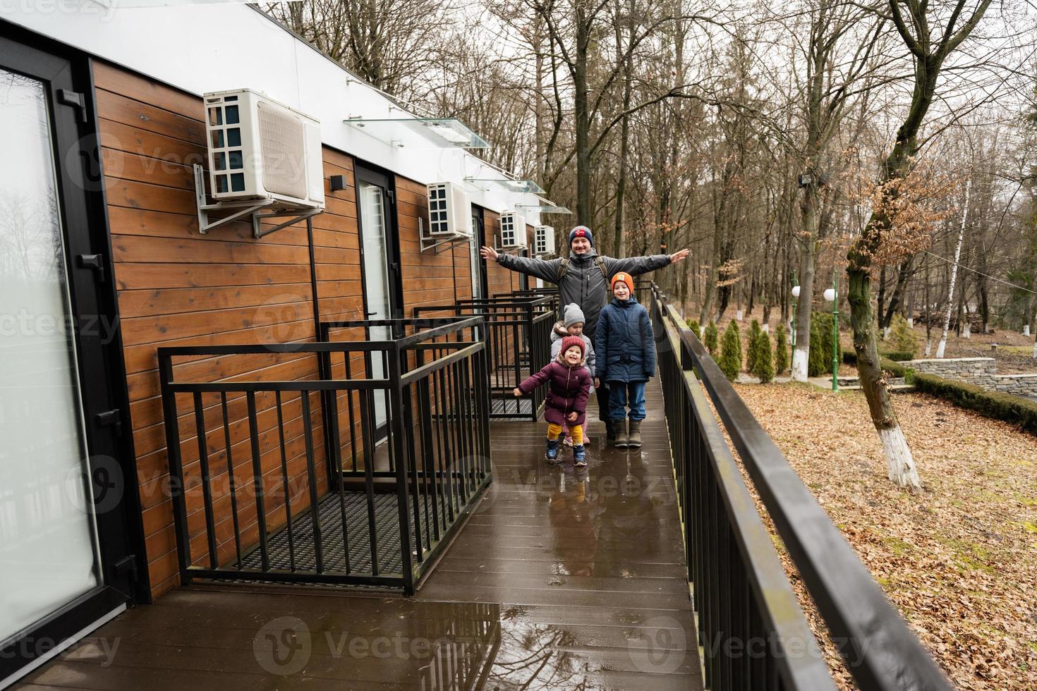 Father with three kids on terrace of one-storey modular houses in spring rainy forest. photo
