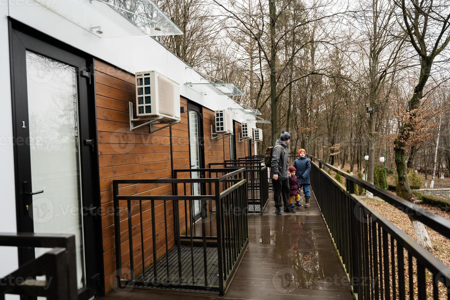 Father with three kids on terrace of one-storey modular houses in spring rainy forest. photo
