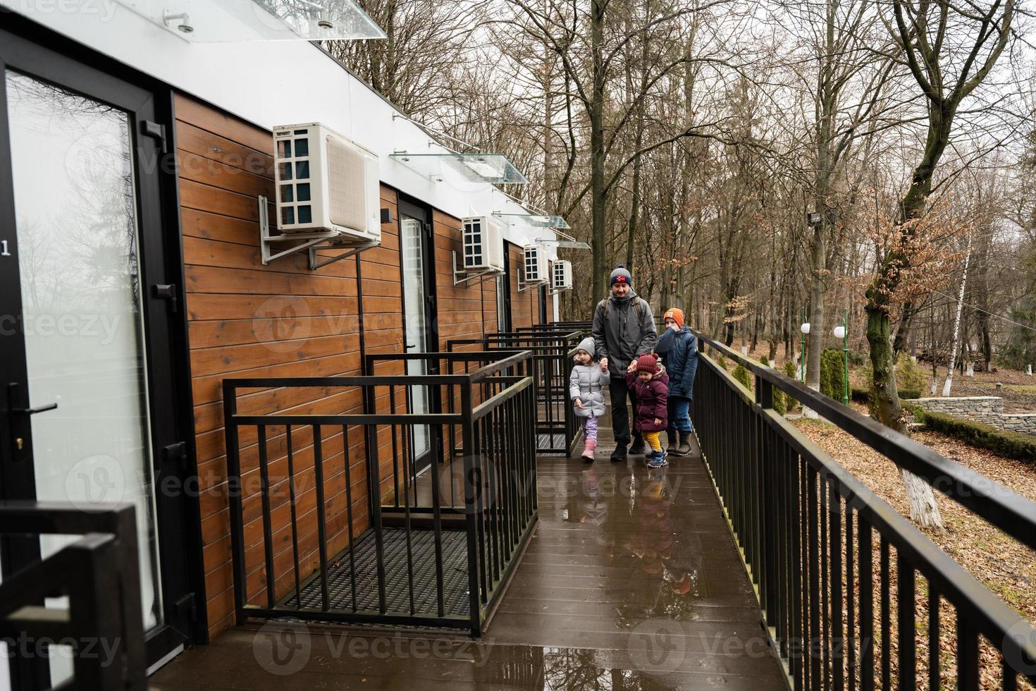 Father with three kids on terrace of one-storey modular houses in spring rainy forest. photo