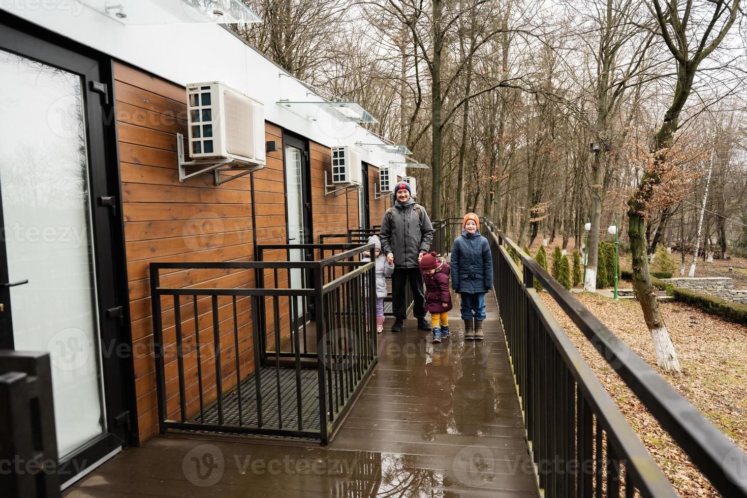 Father with three kids on terrace of one-storey modular houses in spring rainy forest. photo
