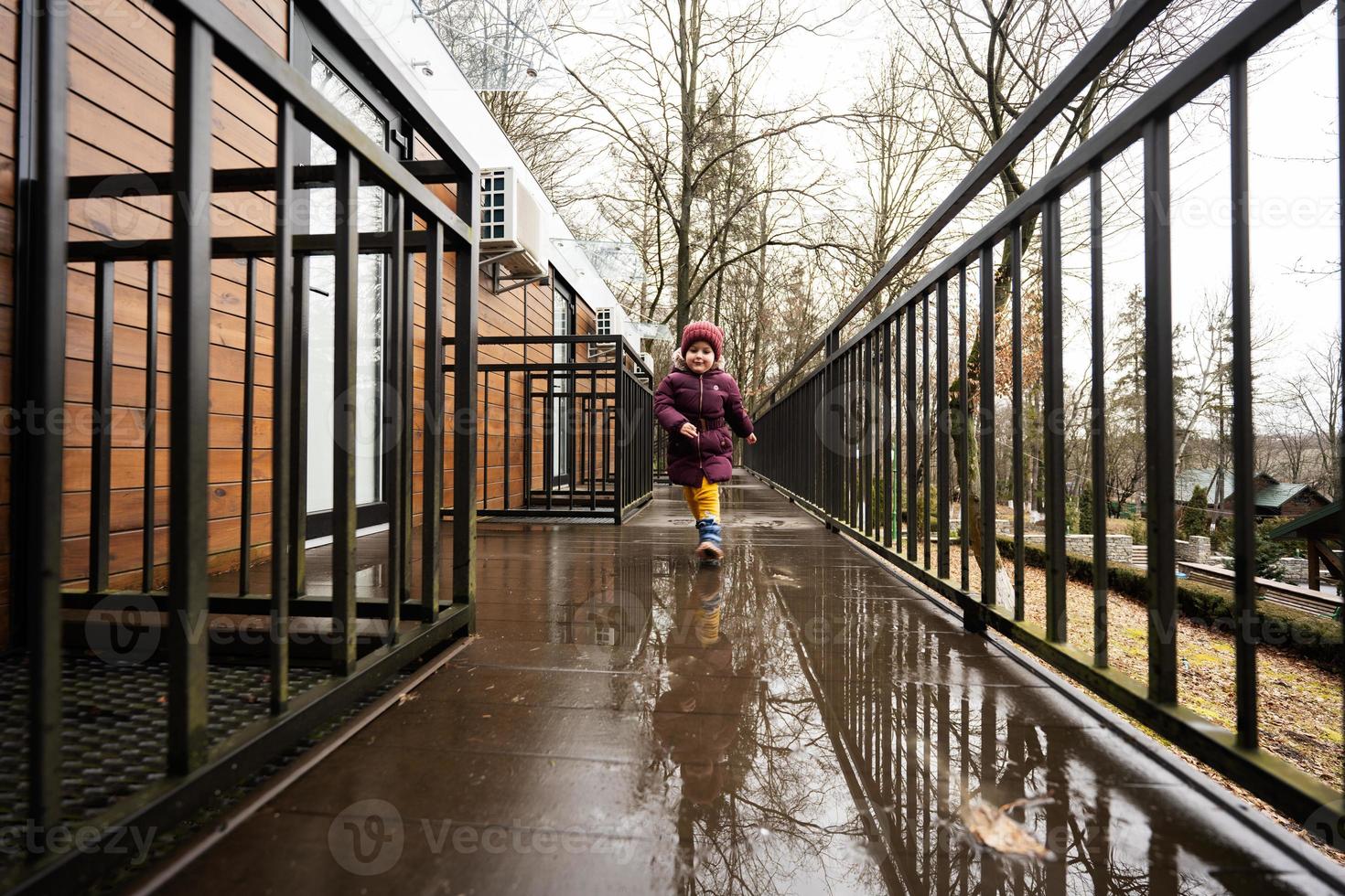 Baby girl running on terrace of one-storey modular houses in spring rainy forest. photo