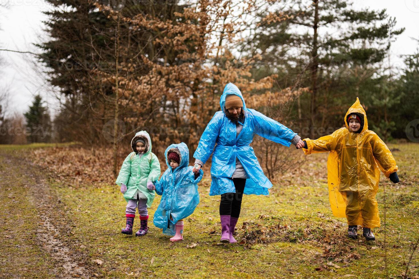 Mother and three children walking in the forest after rain in raincoats together. photo
