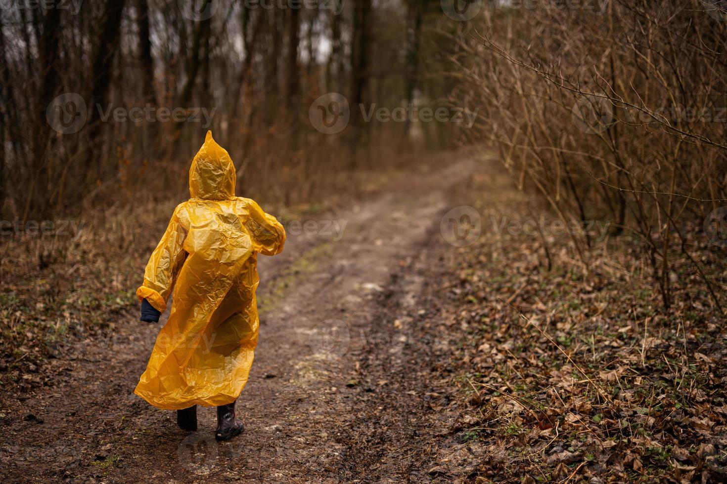 Rear view of boy in yellow raincoat walking in the forest after rain. photo