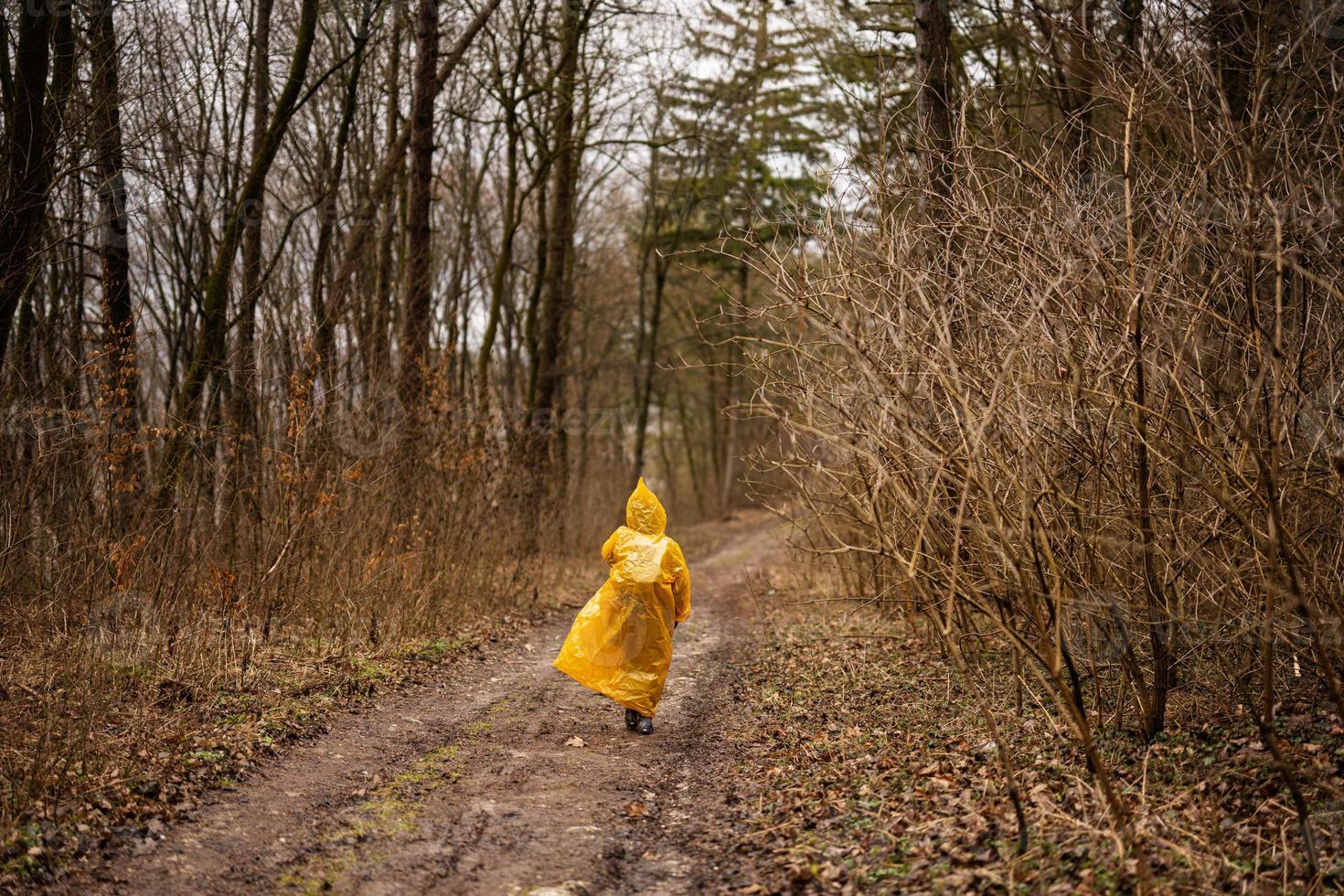 Rear view of boy in yellow raincoat walking in the forest after rain. photo