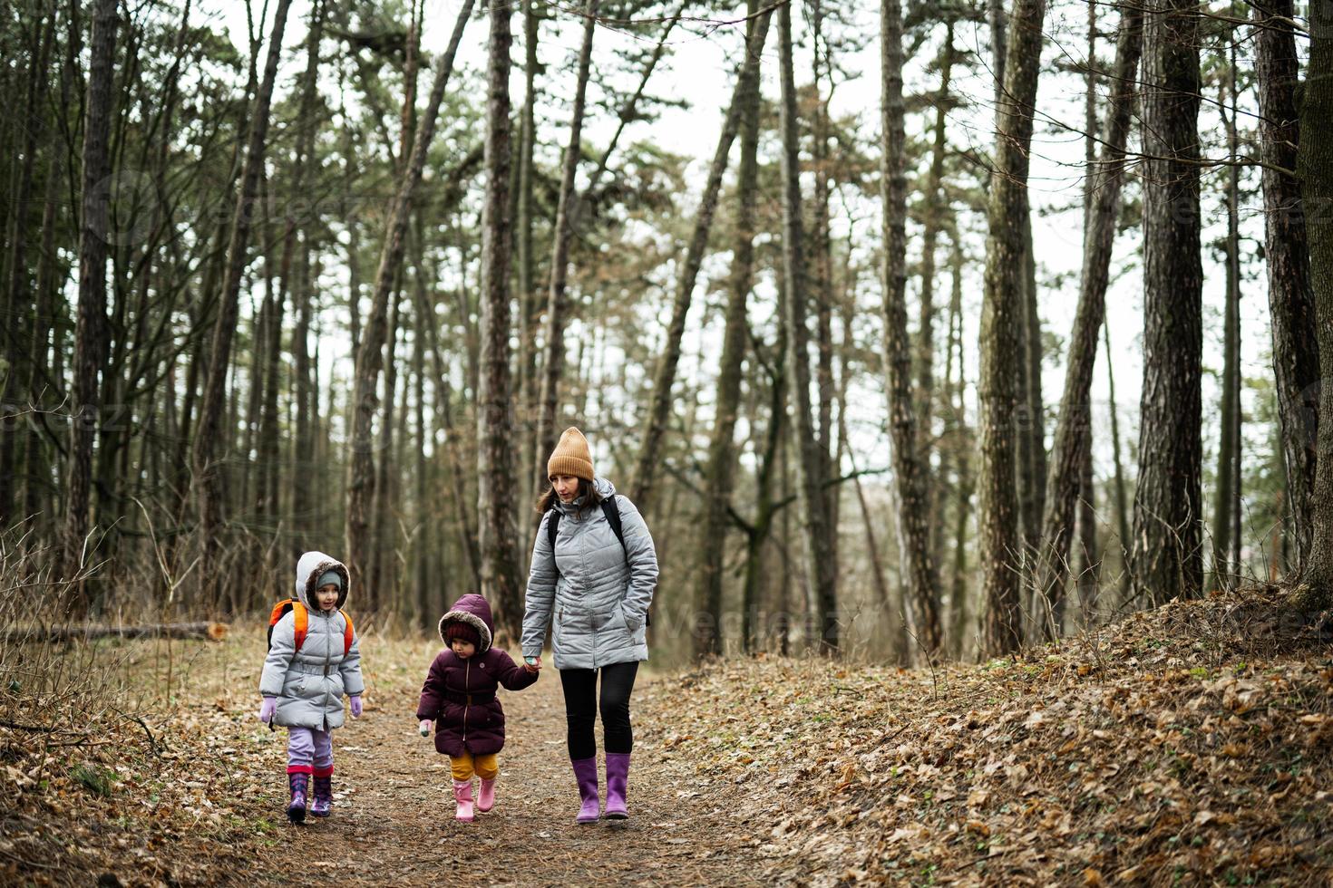 Mother and two daughters with backpacks walking along the forest road together. photo