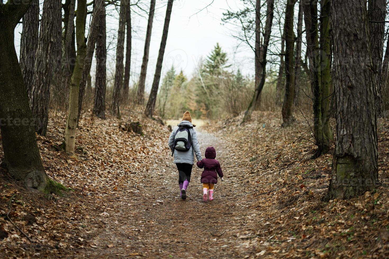 Back of mom with backpack and daughter walking along the forest after rain together. photo