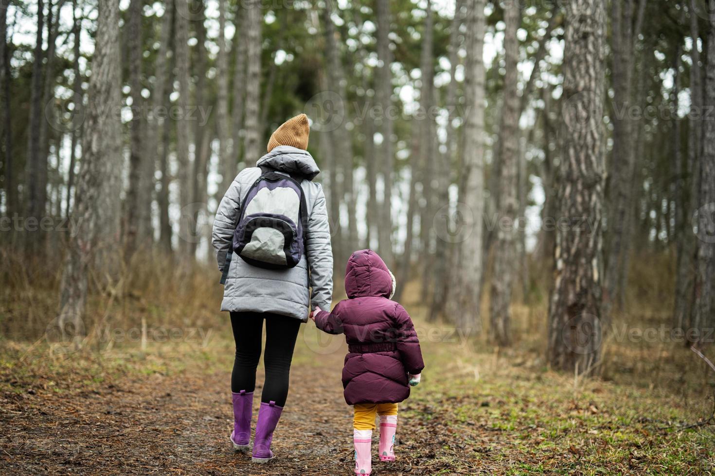 Back of mom with backpack and daughter walking along the forest after rain together. photo