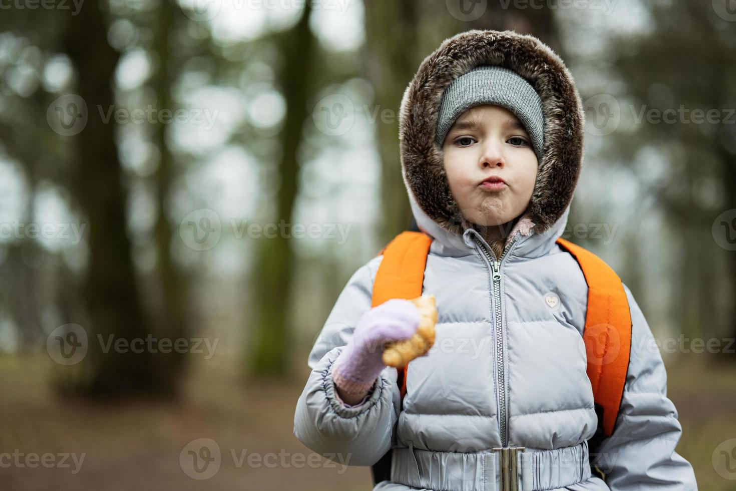 Girl with backpack eating croissant in the forest. photo