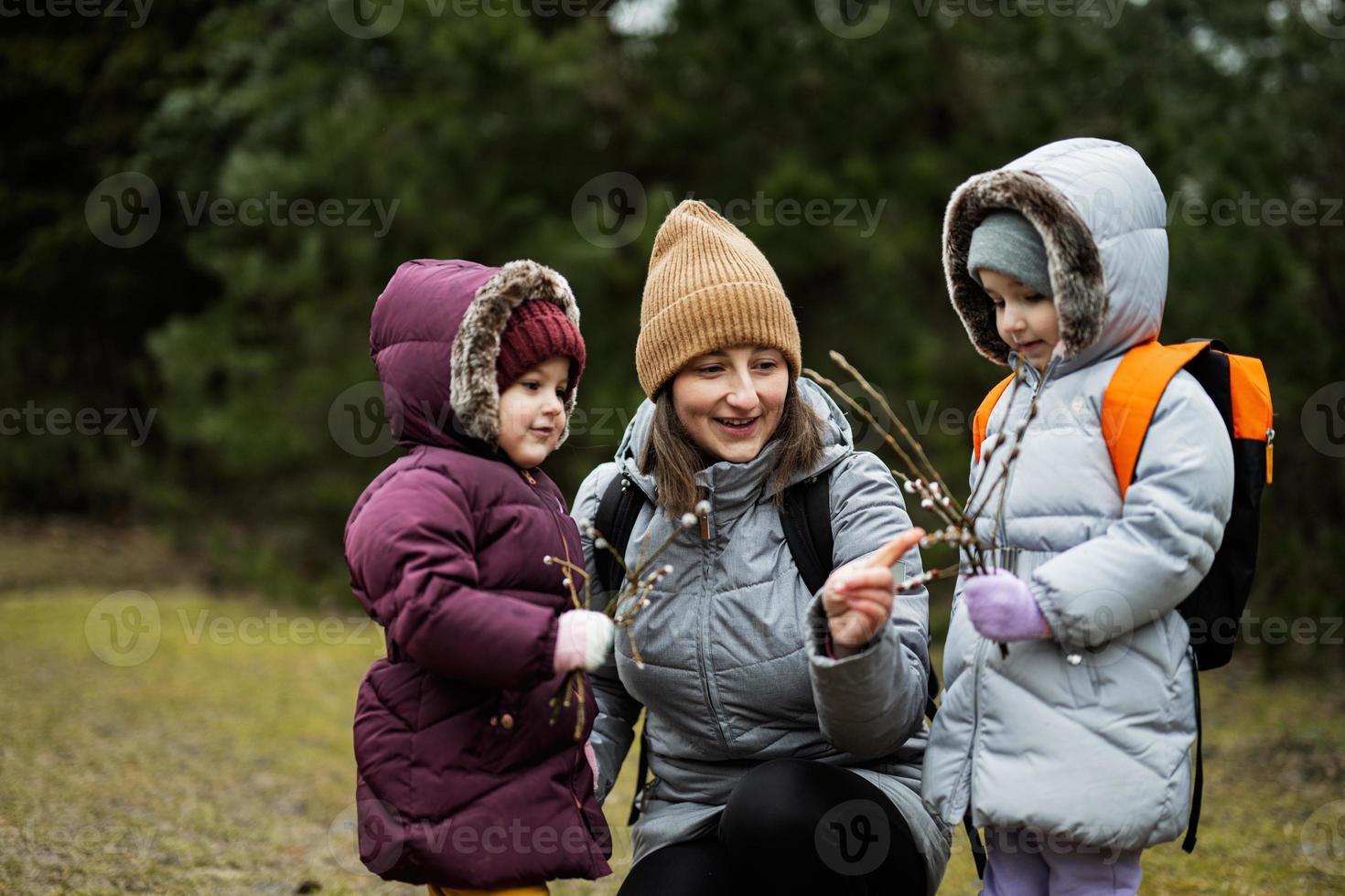 Mother with daughters holding willow twigs in forest. photo