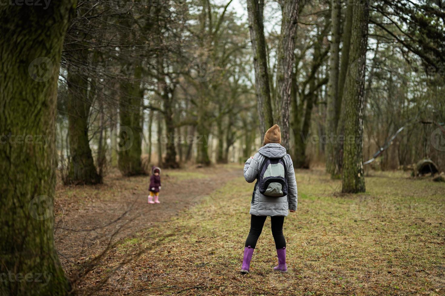 Back of mom with backpack and daughter walking along the forest after rain together. photo