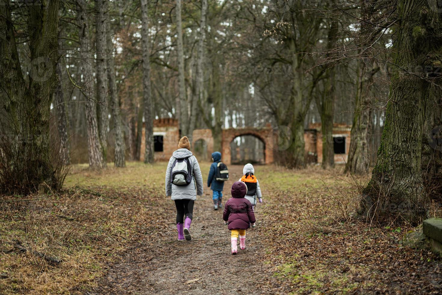 Back of mom and children with backpacks walking along the forest after rain together. photo