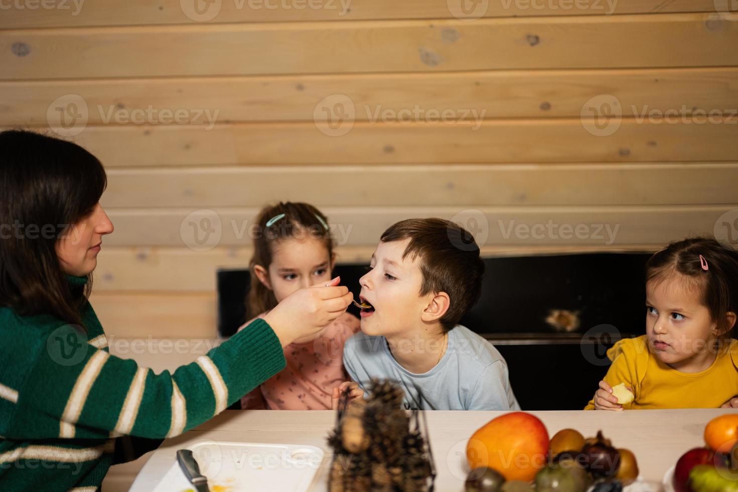 madre con Tres niños comer frutas en de madera país casa en fin de semana. foto
