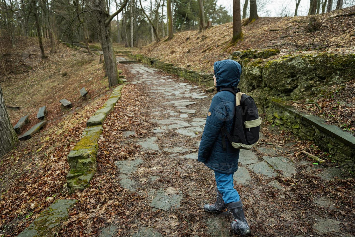 Back of boy with backpack walking along the forest stone road after rain. photo