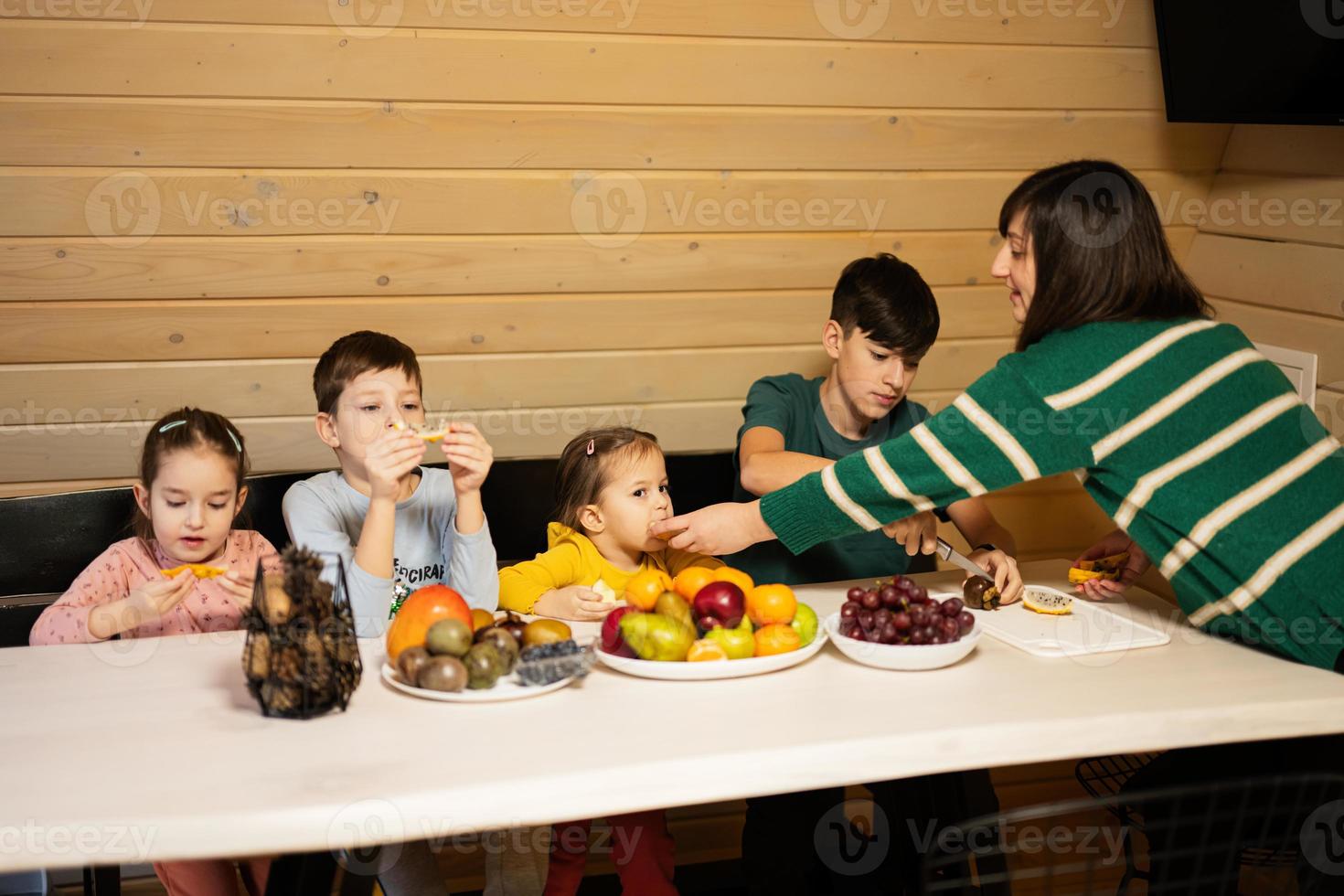 madre con cuatro niños comer frutas en de madera país casa en fin de semana. foto