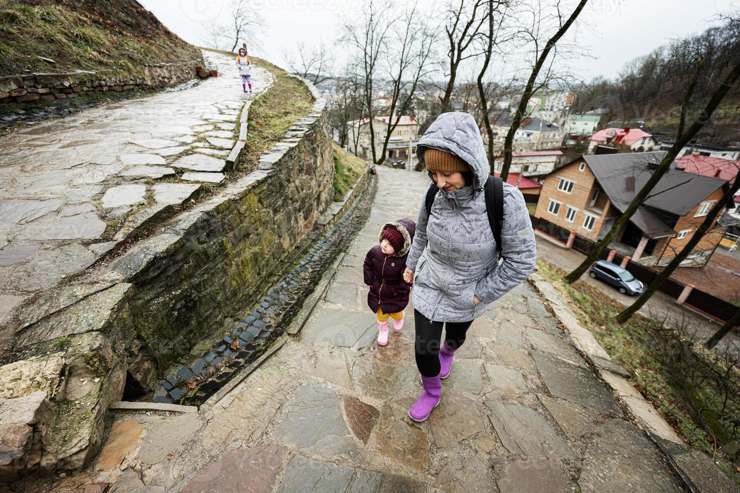 Mother and girls walk up the wet path to an ancient medieval castle fortress in rain. photo