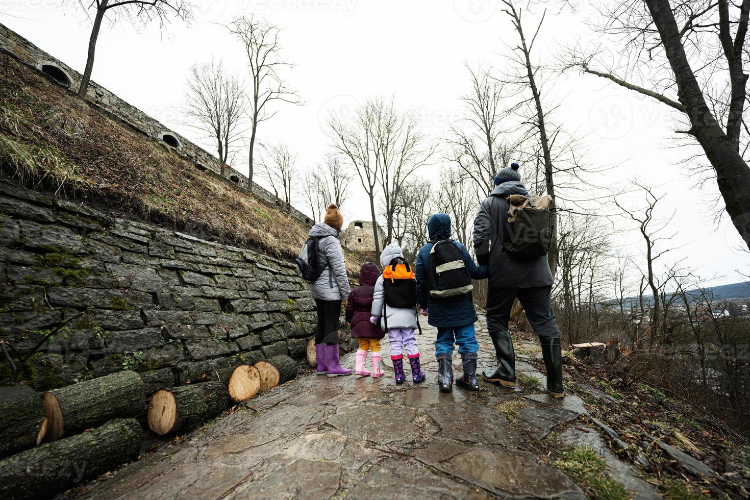 Back of family with three children stand on wet path to an ancient medieval castle fortress in rain. photo