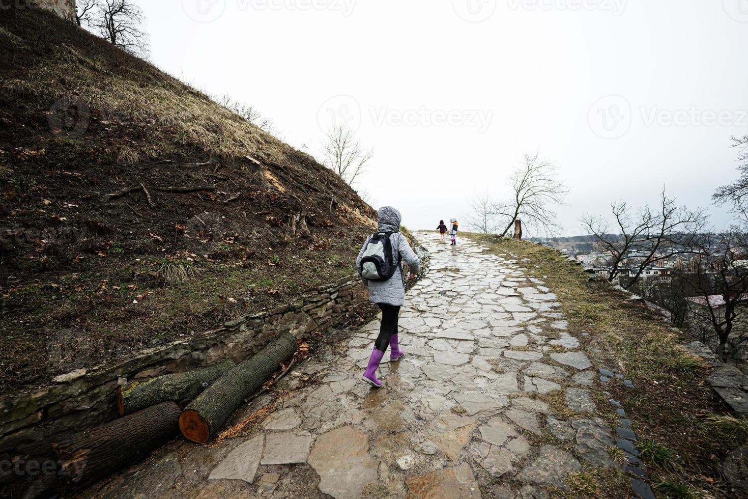 Mother and girls walk up the wet path to an ancient medieval castle fortress in rain. photo