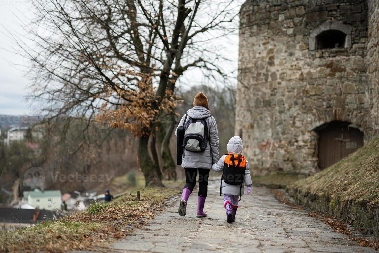 Mother with daughter walk down wet path to an ancient medieval fortress in rain. Terebovlia castle, Ukraine. photo