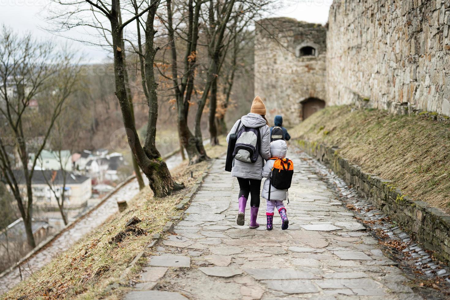 Mother with daughter walk down wet path to an ancient medieval fortress in rain. Terebovlia castle, Ukraine. photo