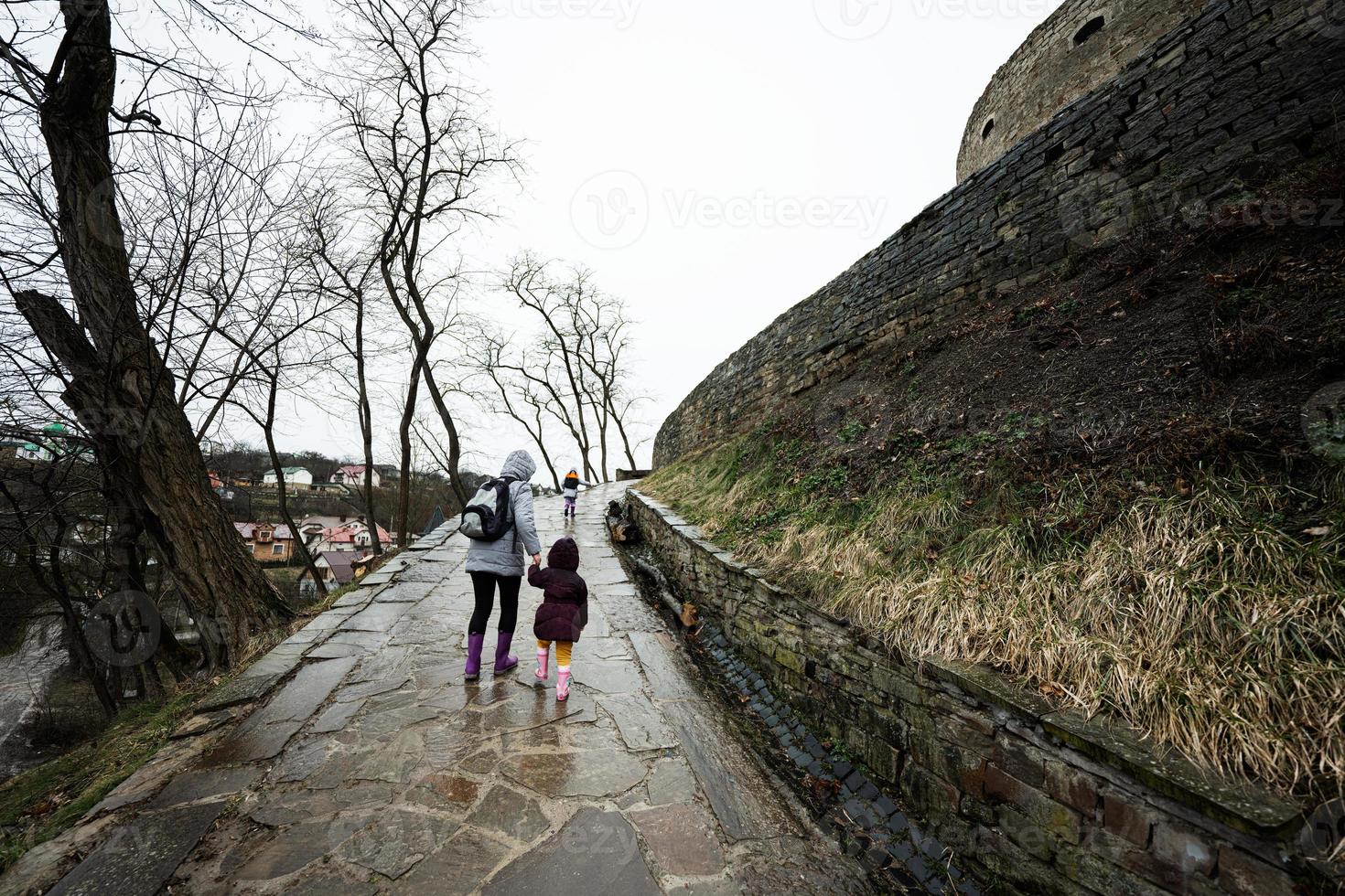 Mother and girls walk up the wet path to an ancient medieval castle fortress in rain. photo