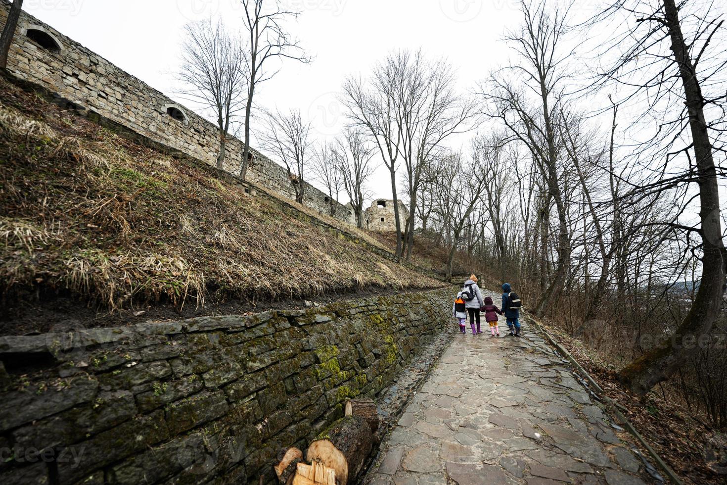 Back of mother and children walk up the wet path to an ancient medieval castle fortress in rain. photo