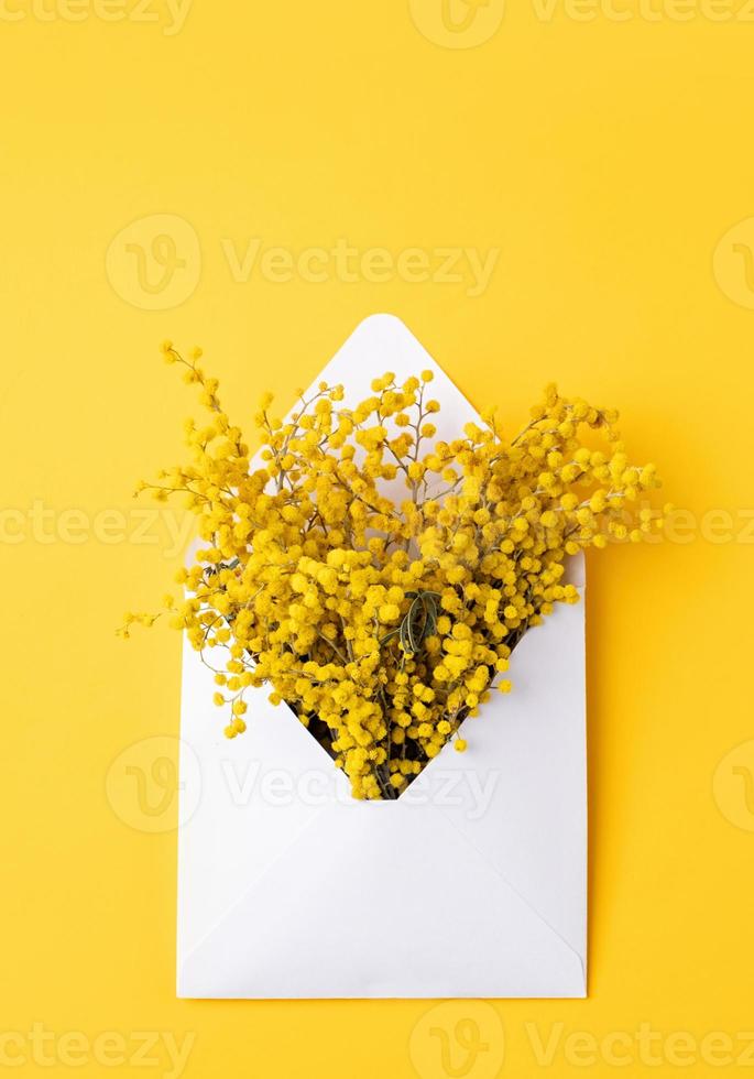 Opened white envelope with yellow mimosa flowers on yellow background, mockup design photo