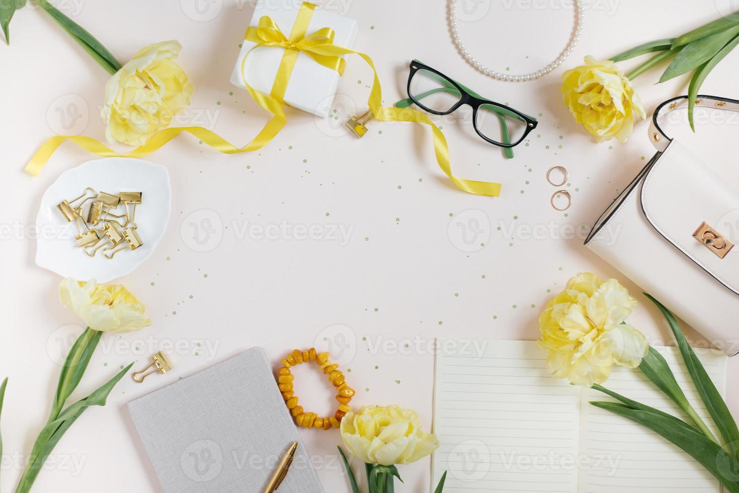 Accessories for a woman blogger on a light background with a handbag, spring flowers yellow tulips, a notebook and a pen, accessories, glasses, a gift. Spring workplace concept top view. Flat lay. photo
