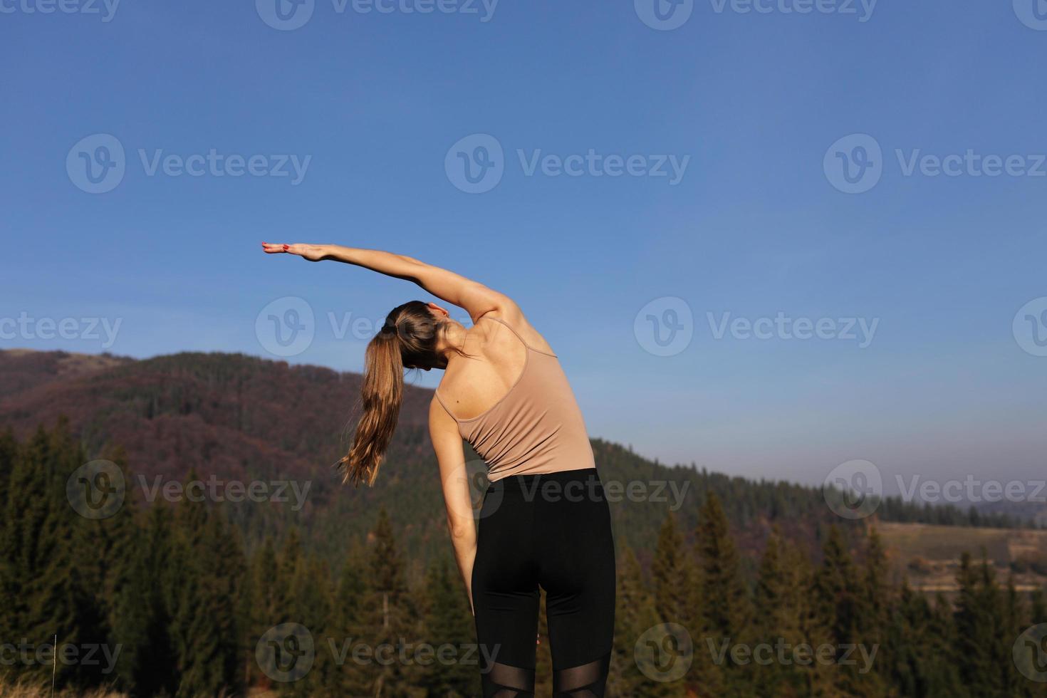 Young athletic woman stretching before intense morning workout at sunset or sunrise in beautiful mountain location. The concept of energy, health and harmony during sports photo