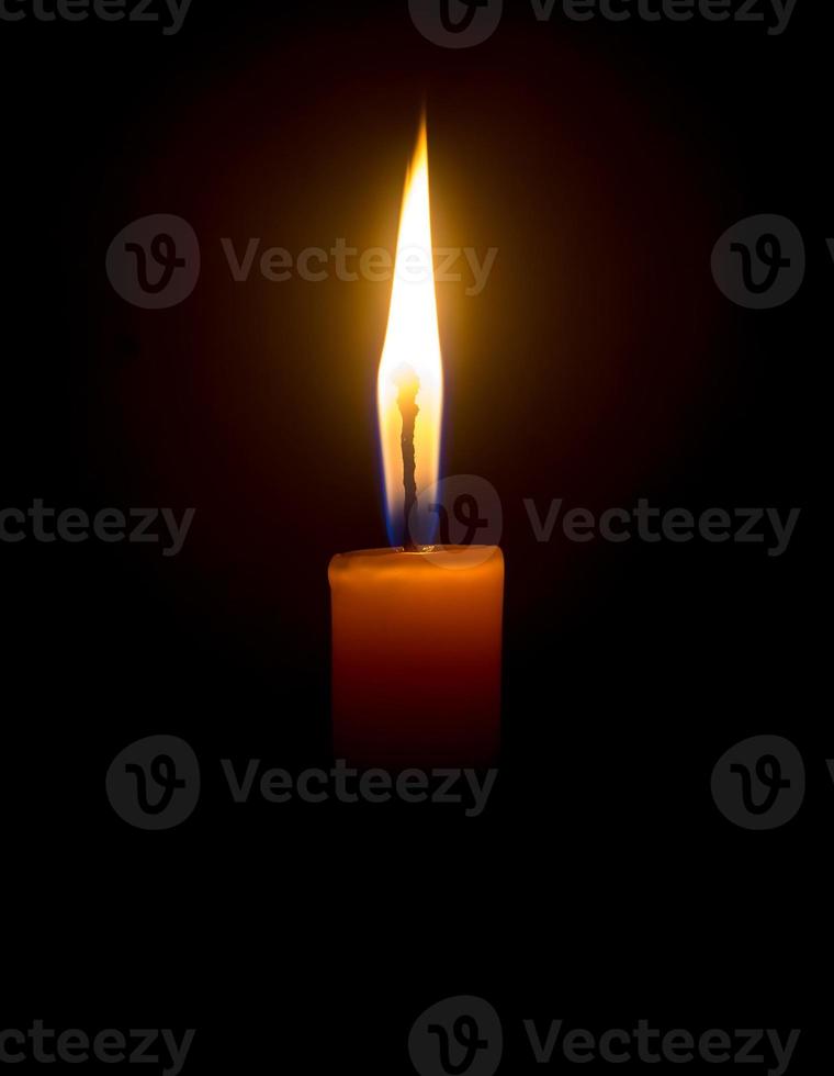 A single burning candle flame or light glowing on an orange candle on black or dark background on table in church for Christmas, funeral or memorial service with copy space photo