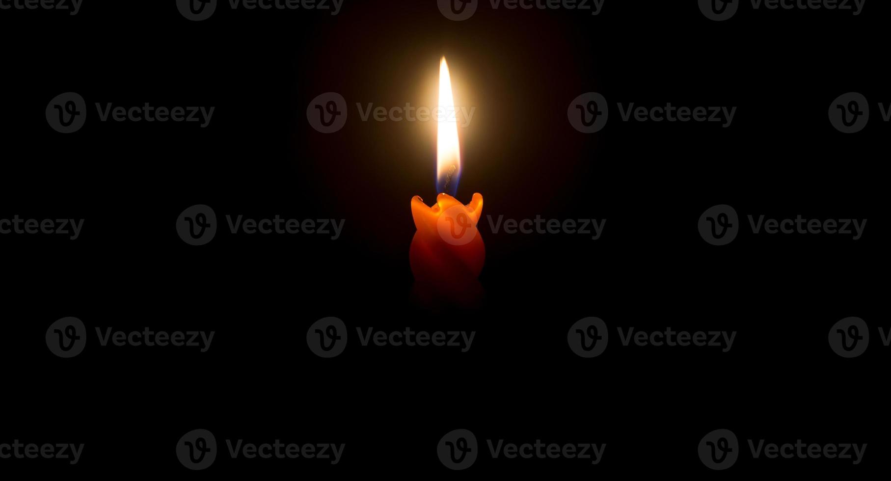 A single burning candle flame or light glowing on a beautiful spiral orange candle on black or dark background with copy space for adding text on table in church for Christmas photo