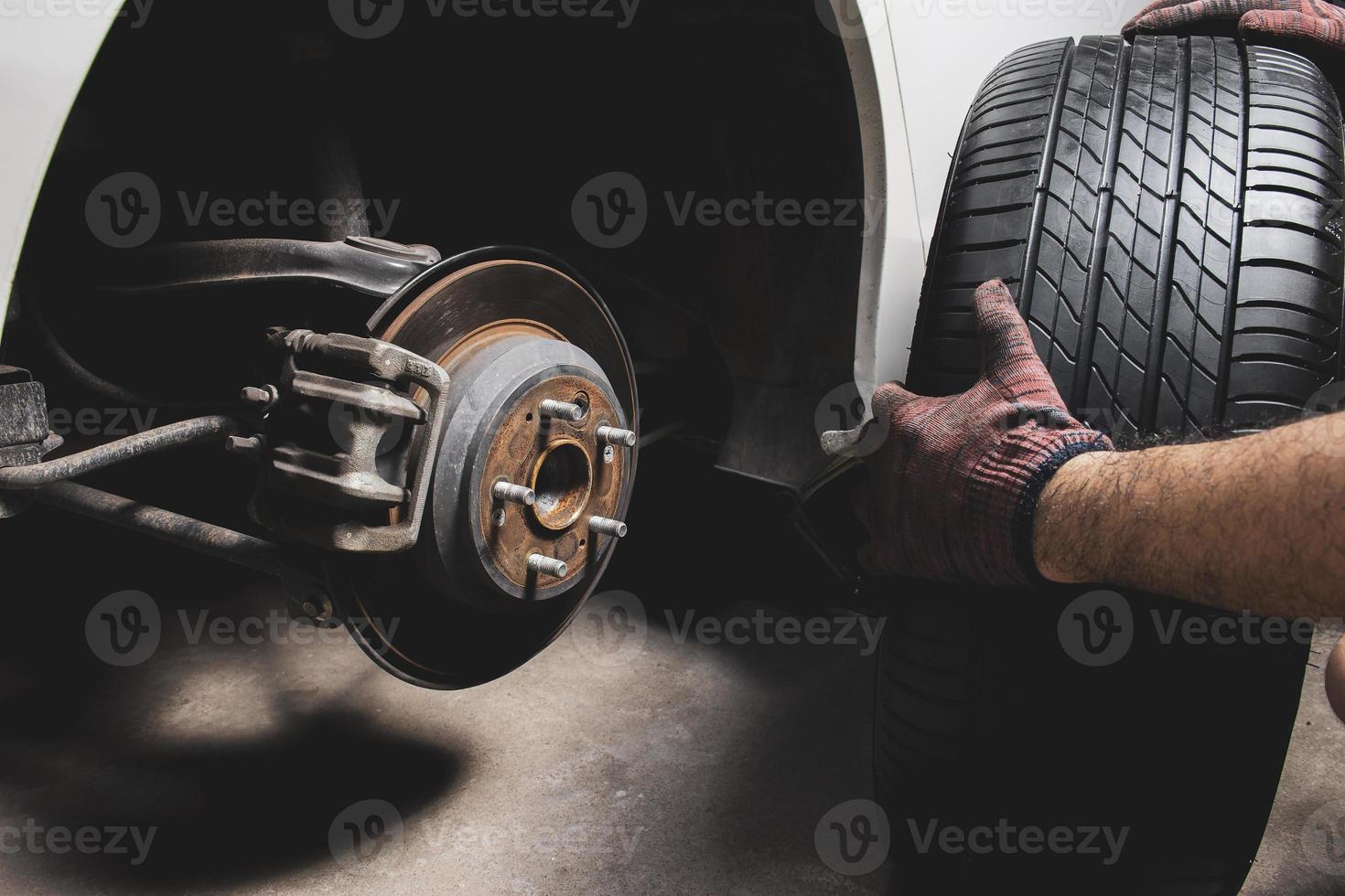 un mecánico es quitando un rueda desde un coche a reemplazar un de repuesto rueda o reparar el freno sistema en el auto reparar cochera. foto