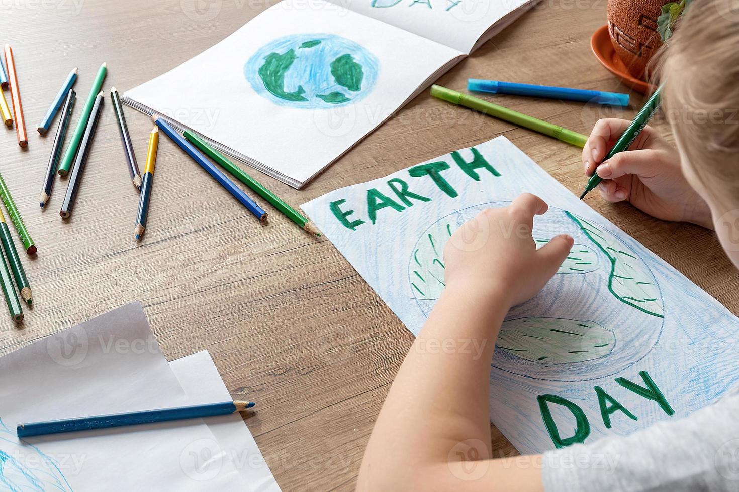 A child at home at the table draws the planet Earth with a world map with multi-colored pencils and felt-tip pens on white paper. Peace and earth day concept. photo