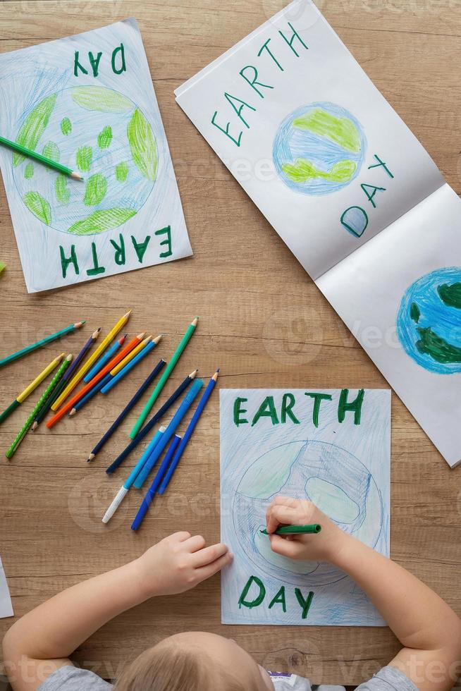 A child at home at the table draws the planet Earth with a world map with multi-colored pencils and felt-tip pens on white paper. Peace and earth day concept. photo