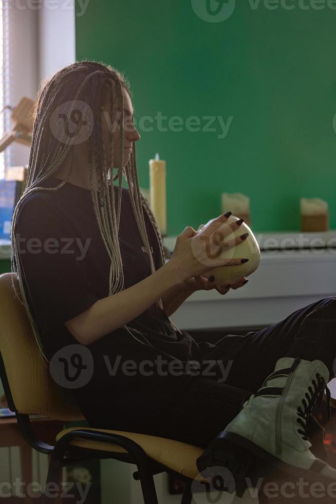 A young bright girl in dark clothes, with dreadlocks on her head, holds a skull in her hands. Generation z, gothic style photo