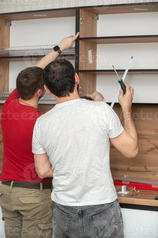 Two craftsmen, furniture makers and assemblers, are installing a modern kitchen in a home, tools in their hands. Concept furniture to order, improvement of living conditions, repair photo