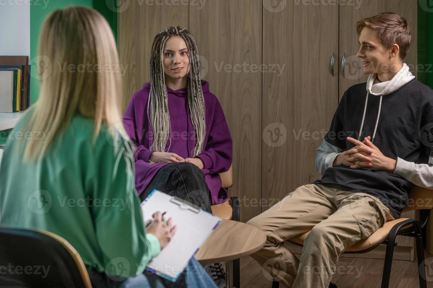 A female psychologist works in her office with a young married couple. In the hands of a specialist are the notes that she makes during the consultation photo