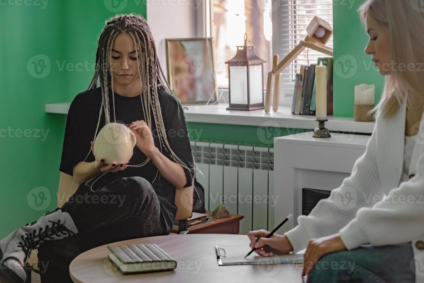 a female psychologist works in her office with a young client with dreadlocks on her head, who is holding a mock-up of a skull. Problems of generation z in life, in communication. photo