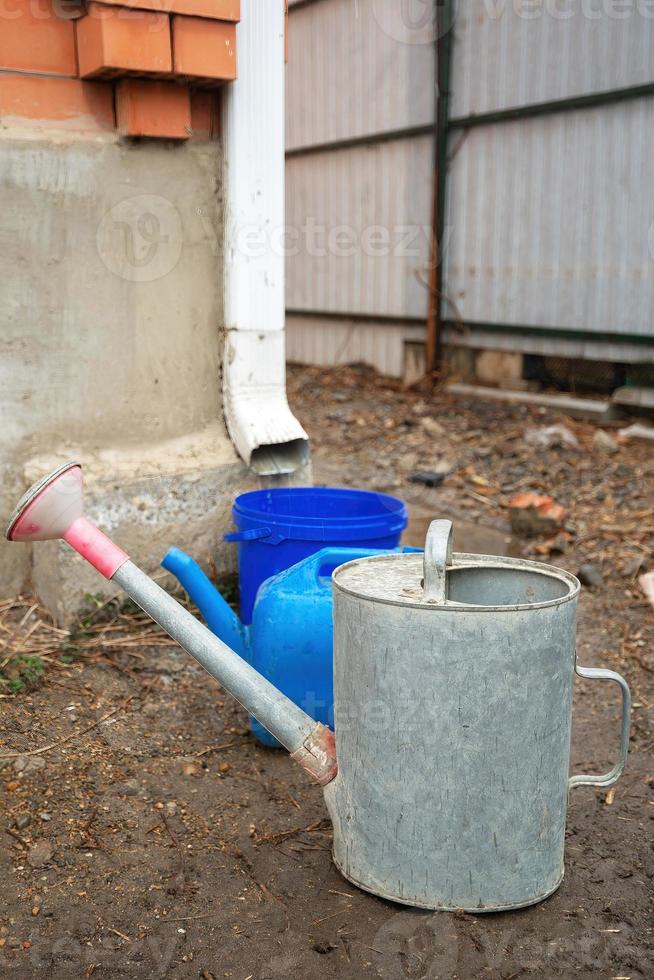 Collection of rainwater in different canisters buckets, watering cans in the yard of his house near the downpipe for further use and watering, space for text photo