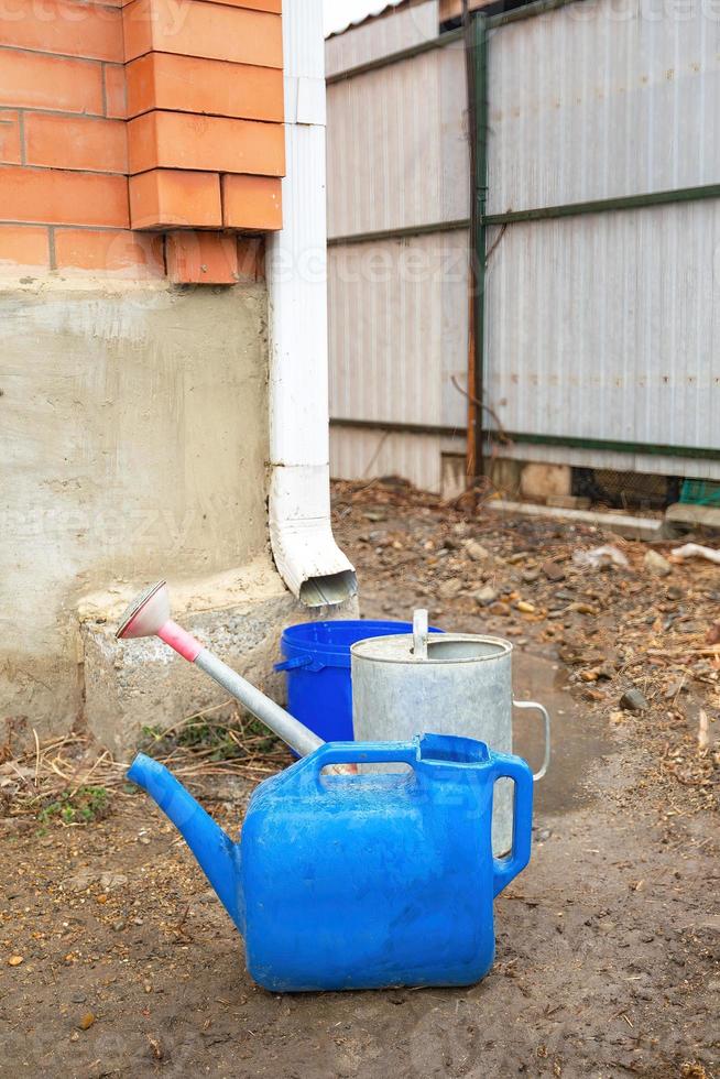 Collection of rainwater in different canisters buckets, watering cans in the yard of his house near the downpipe for further use and watering, space for text photo