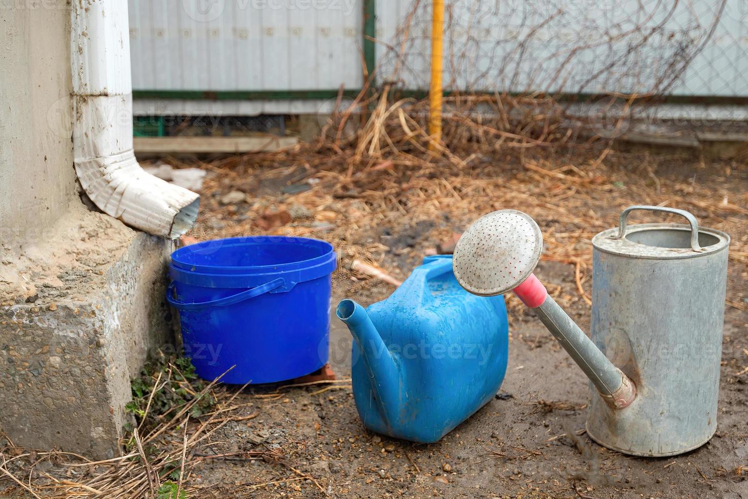 Collection of rainwater in different canisters buckets, watering cans in the yard of his house near the downpipe for further use and watering, space for text photo