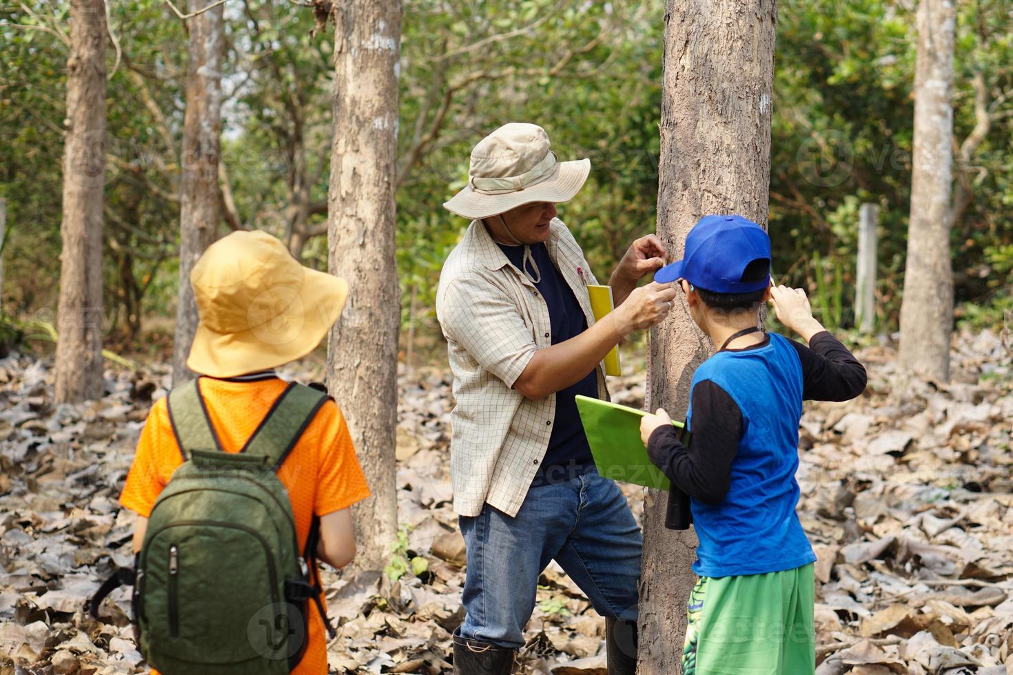 Asian man teacher is teaching botanical plants with students. Outdoor classroom. Summer camp activity. Concept, Learning by doing. Active learning.Real life experience. Nature survey. photo