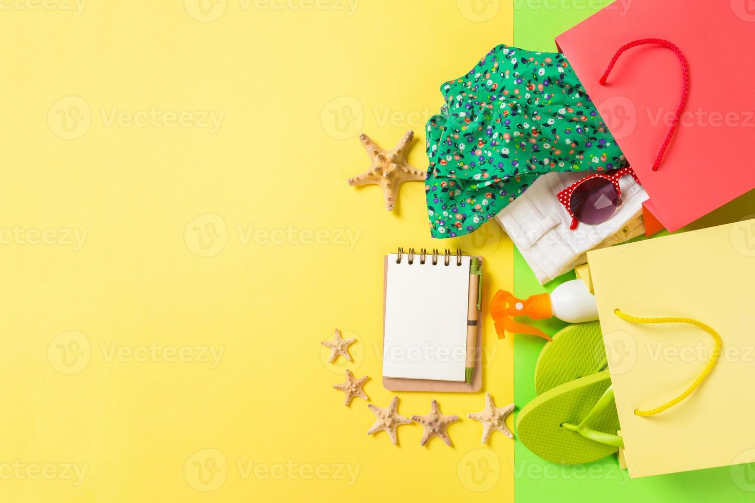 Summer concept of colourful shopping bags full of clothes. Gift bags with T-shirt, denim shorts, flip flops, notebook and bottle of sunscreen. Summer wishlist concept. Top view copy space photo