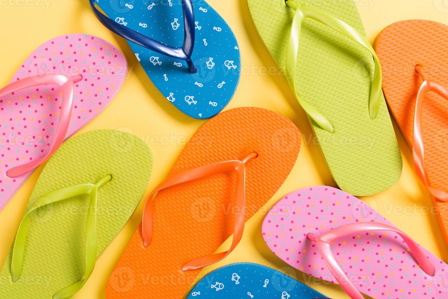 many colored flip flops on yellow background. Copy space top view photo