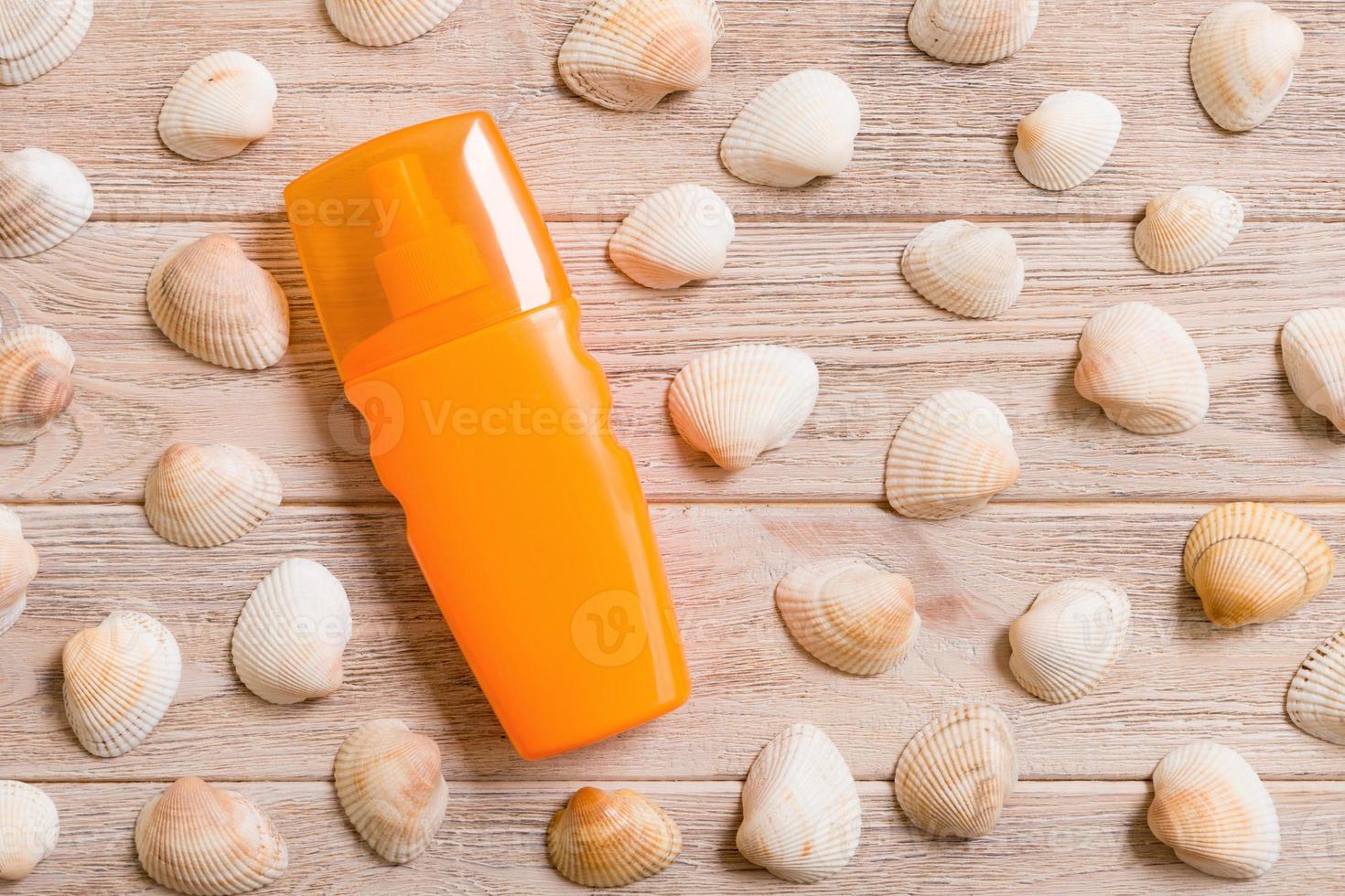 Top view of sunscreen bottle with seashells on wooden board background with copy space. flat lay concept of summer travel vacation photo