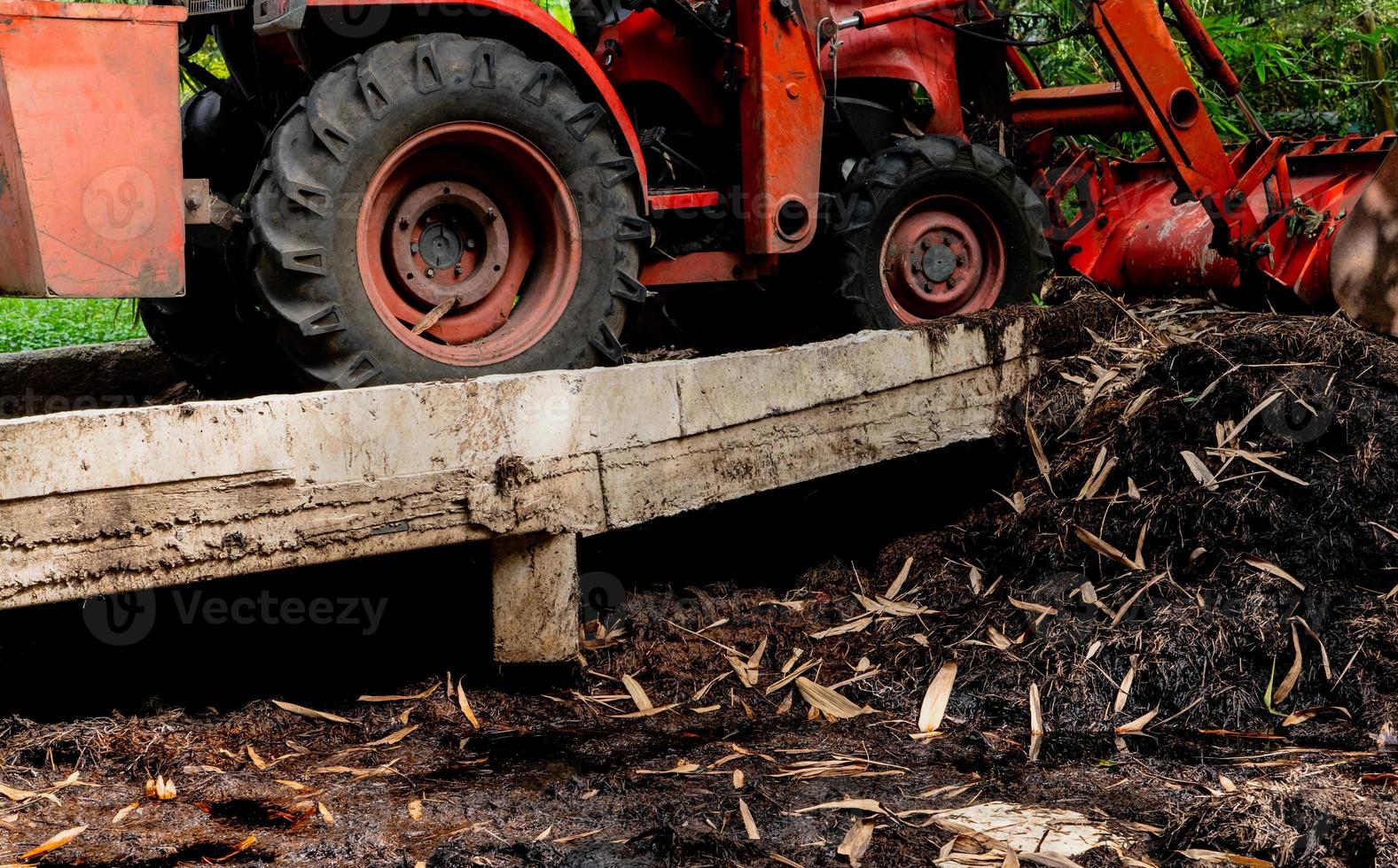 Selective focus on orange tractor working at compost pile in organic garden. Organic gardening. Decomposing plant pile. Recycling organic materials. Agricultural machinery in agriculture farm. photo