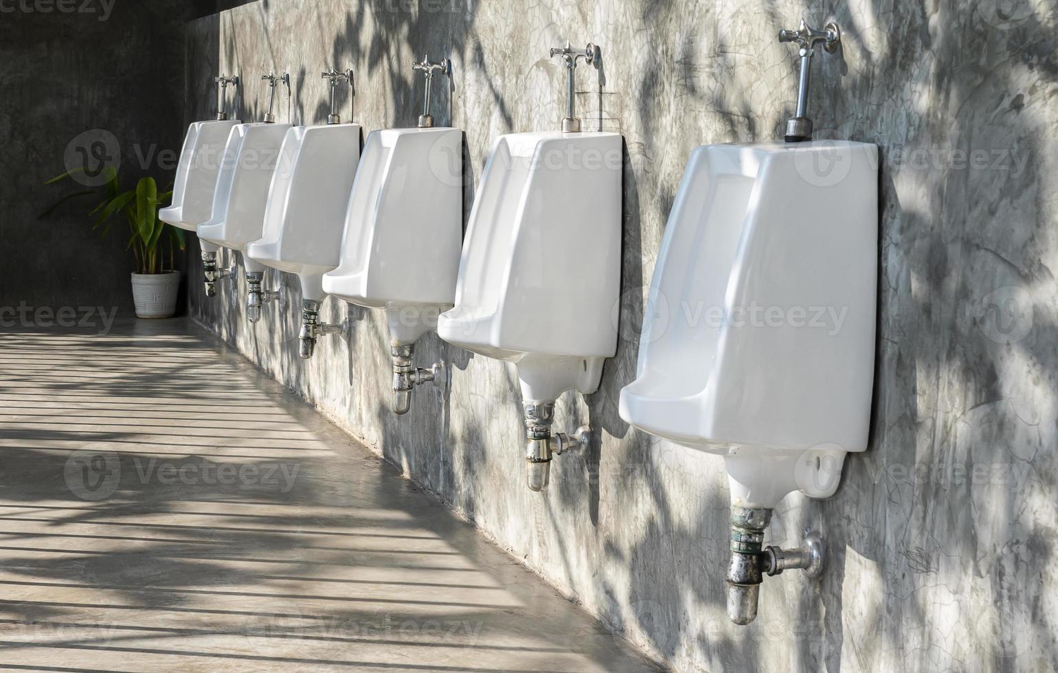 Men's room with white porcelain urinals in line in gas station photo