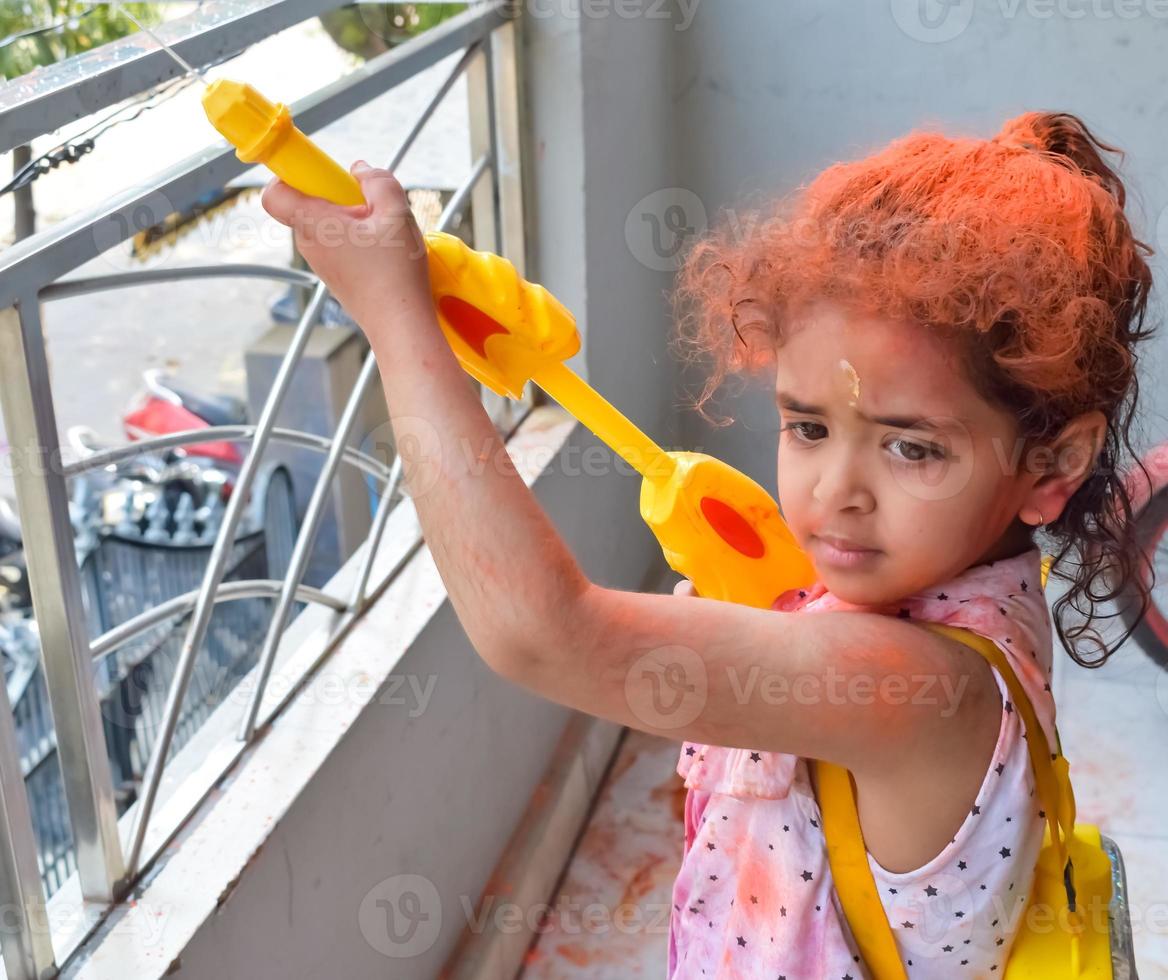 Sweet little Indian girl playing colours on Holi festival, holding pichakaree full of colours, Holi festival celebrations in Delhi, India photo