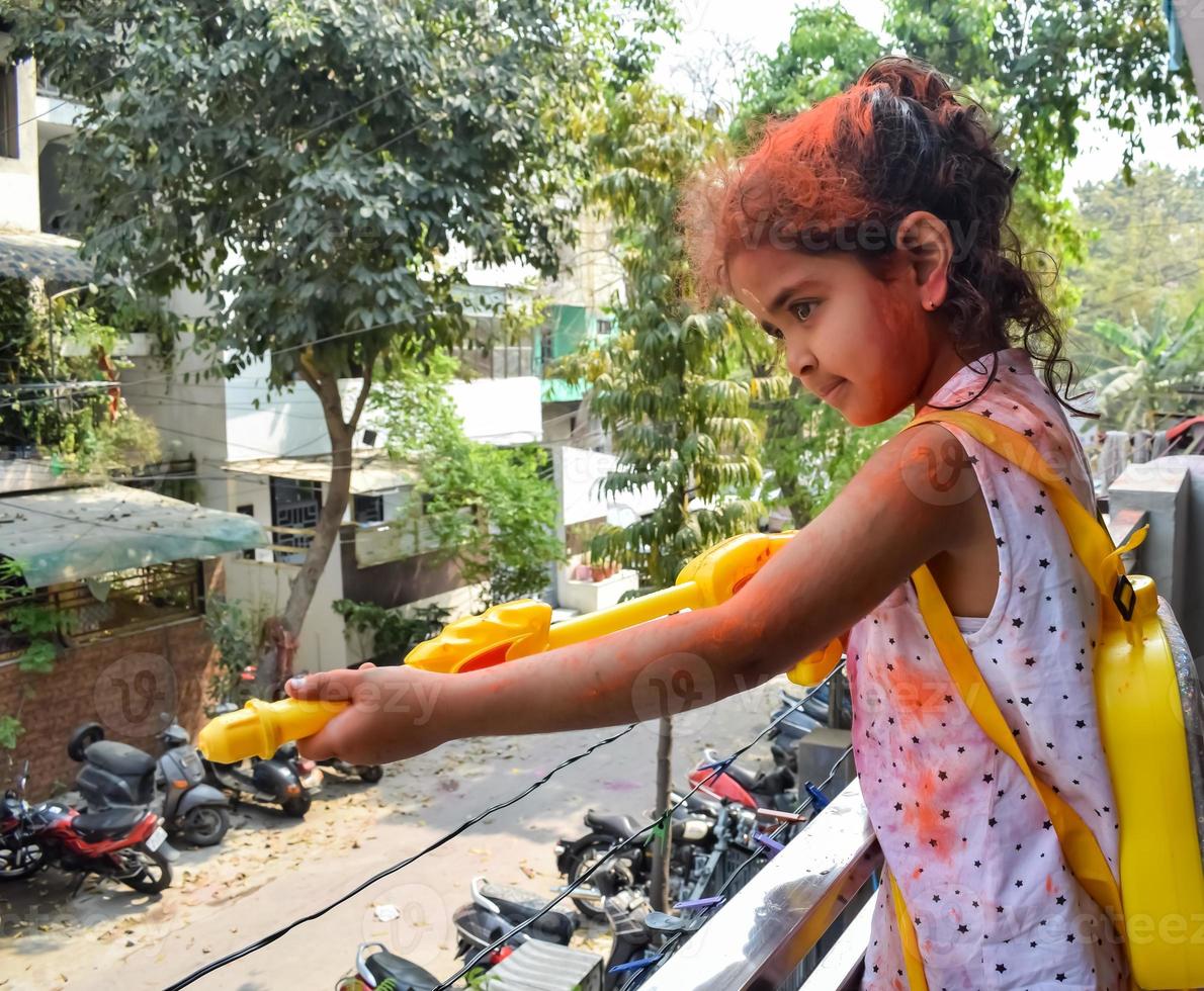 Sweet little Indian girl playing colours on Holi festival, holding pichakaree full of colours, Holi festival celebrations in Delhi, India photo