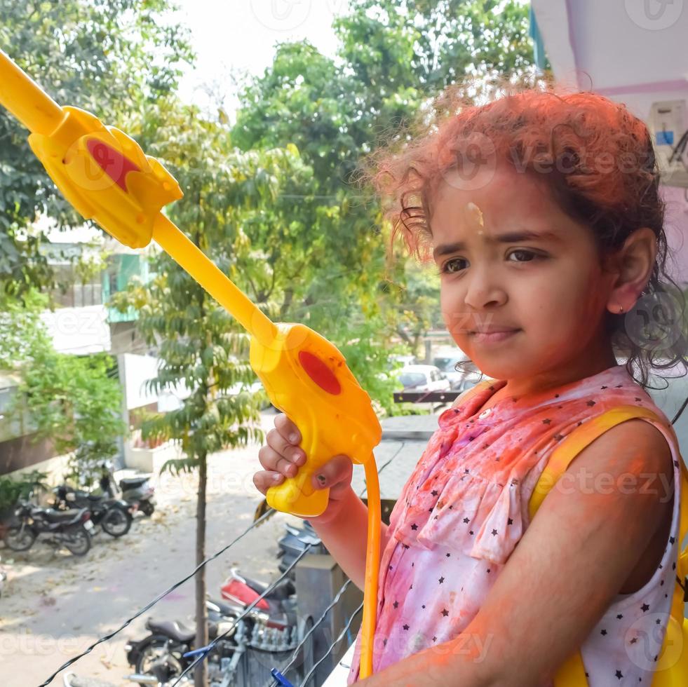 dulce pequeño indio niña jugando colores en holi festival, participación pichakaree lleno de colores, holi festival celebraciones en Delhi, India foto